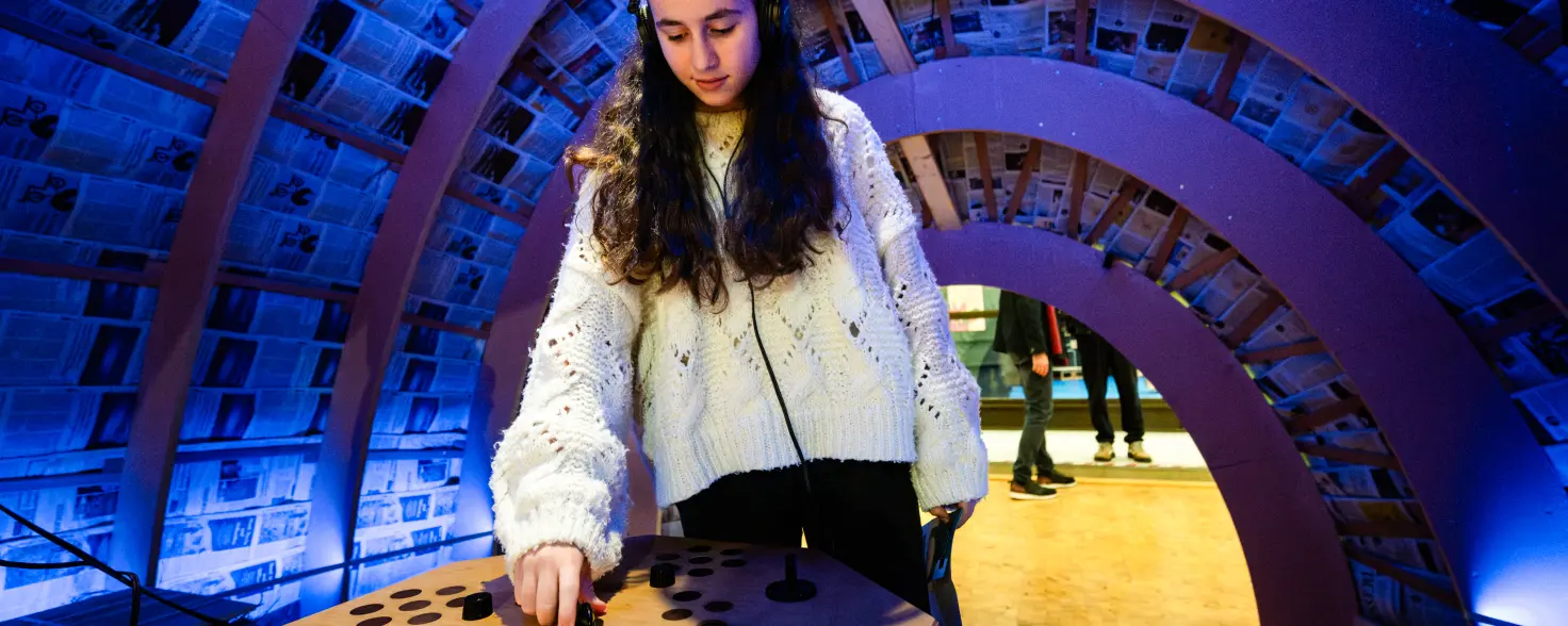 GASAG Umwelt€uro 2026:Person mit Kopfhörern nutzt eine interaktive Klangstation in einer blau beleuchteten Ausstellung im FEZ-Berlin.