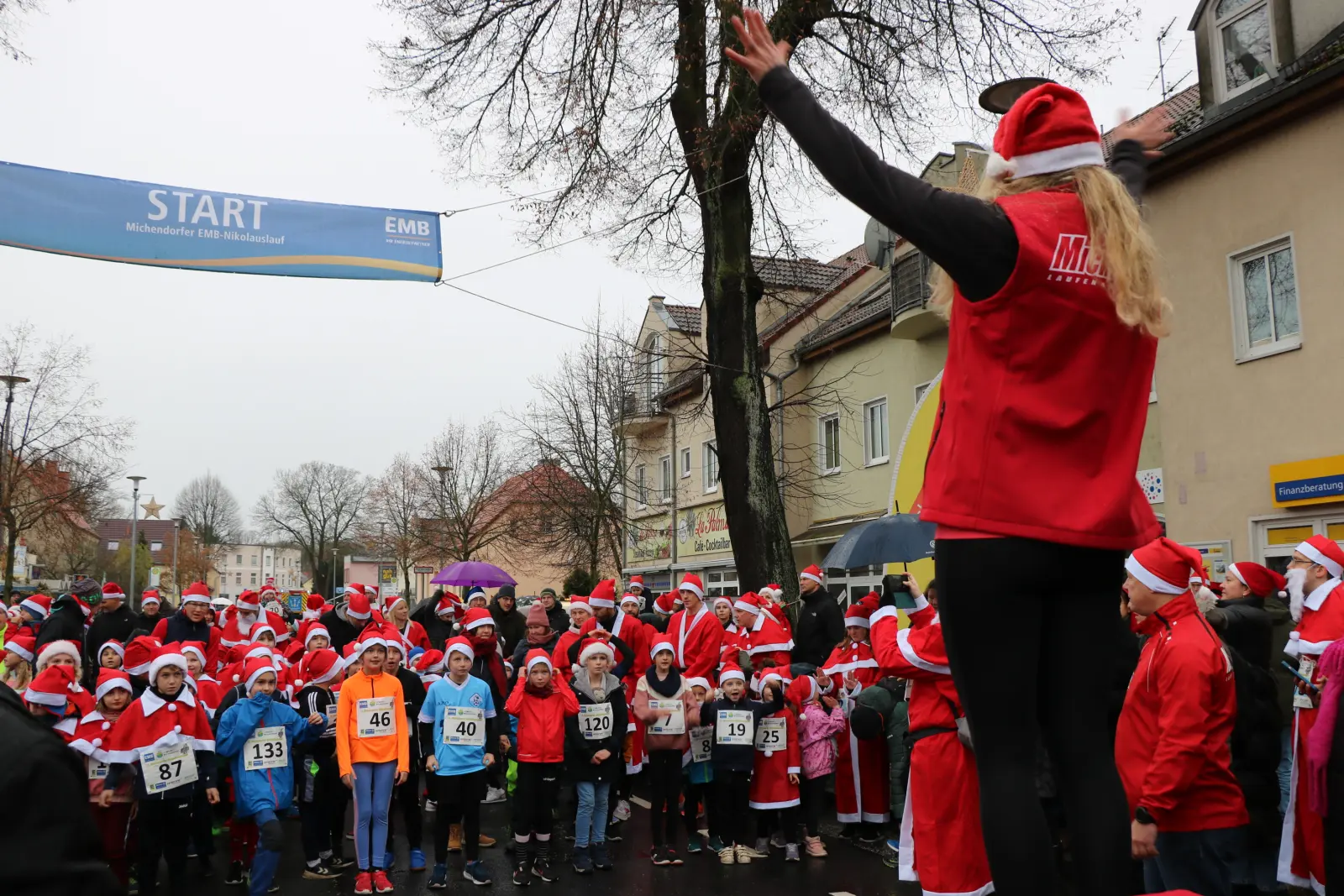 Eine Frau mit roter Zwipfelmütze animiert die Kinder zum Aufwärmen bevor der Lauf losgeht