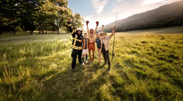 Eine Gruppe von fünf Mitgliedern unterschiedlicher Vereine steht auf einer sonnigen Wiese und hebt die Arme in die Höhe. 