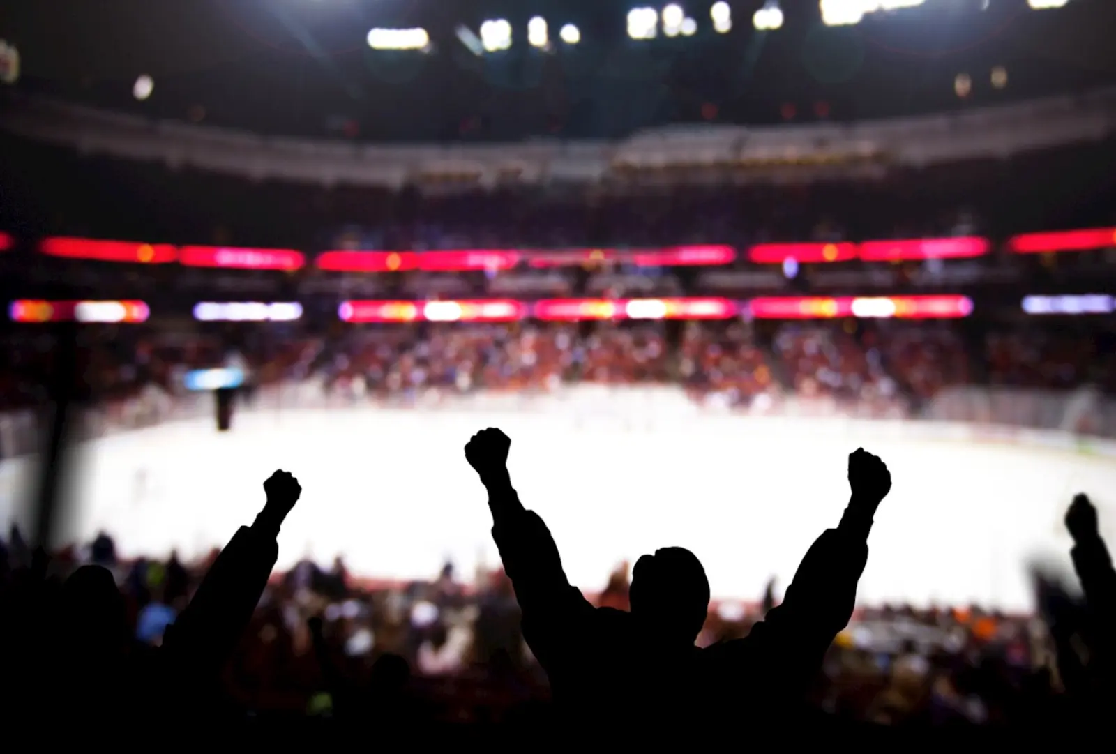 Dunkle Silhouetten von Fans jubeln in die Luft in einem Eishockey-Stadion.