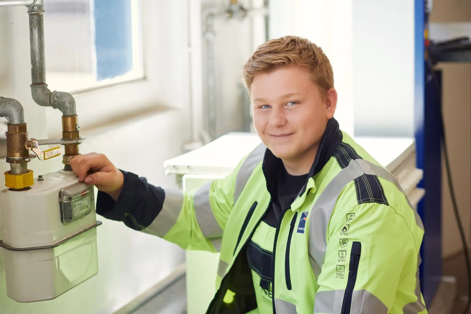 Ein junger Mann in Arbeitskleidung steht neben einem Gaszähler