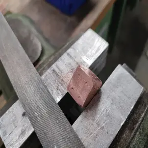 Ein kupferfarbener Metall-Würfel steck in einem Schraubstock