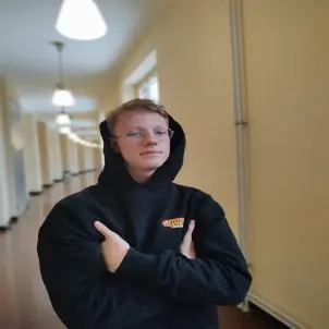 Ein Junge mit schwarzem Kapuzenpullover verschränkt die Arme und schaut in die Kamera.
