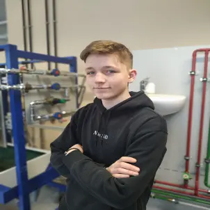 Ein Junge mit schwarzem Kapuzenpullover und verschränkten Armen schaut freundlich in die Kamera.