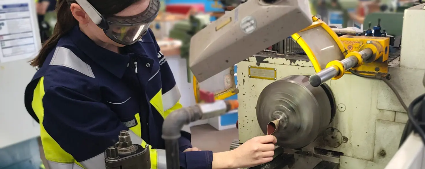 Eine Auszubildende in Uniform und mit Schutzbrille bedient eine Drehmaschine.