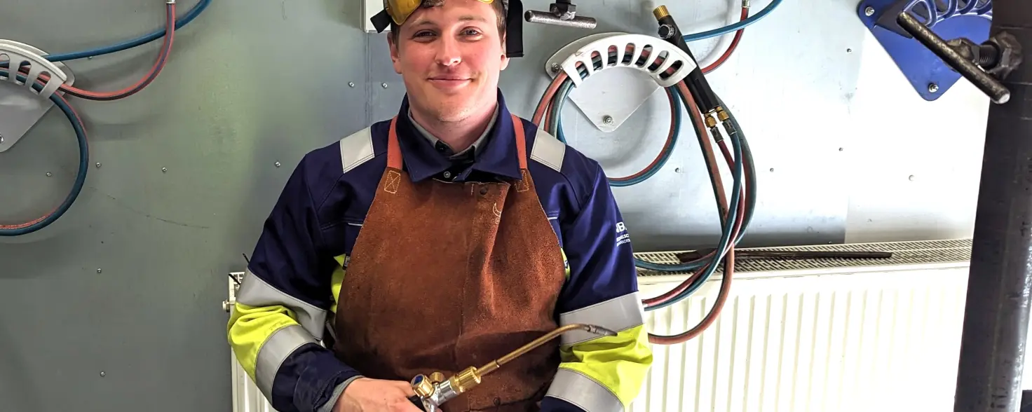 Ein Auszubildender in Uniform sitzt an einer Werkbank und hat ein Schweißgerät in der Hand.