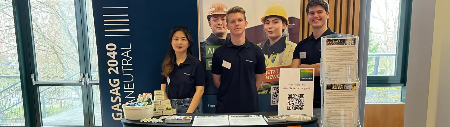 Eine junge Frau und zwei junge Männer stehen hinter einem GASAG Messestand