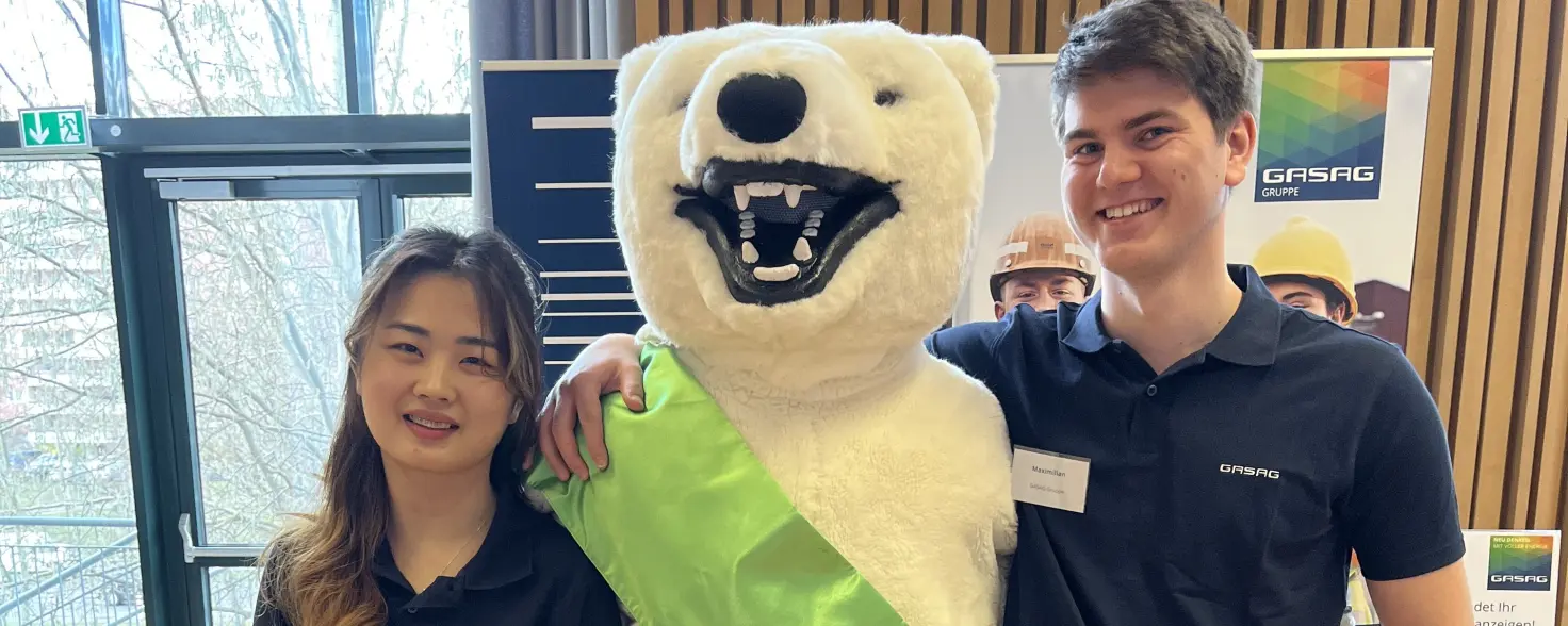Eine junge Frau und ein junger Mann flankieren einen lebensgroßen stehenden Stoff-Eisbär
