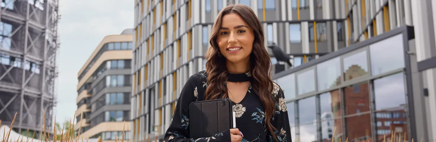 Junge Mitarbeiterin der GASAG-Gruppe hält einen Tablet-PC im Arm und steht vor dem Hauptsitz der GASAG auf dem EUREF-Campus in Berlin-Schöneberg.