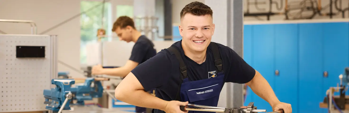 Lächelnder Auszubildender der NBB Netzgesellschaft arbeitet in der Ausbildungswerkstatt der GASAG-Gruppe am Schraubstock.