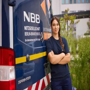 Junge Frau lehnt am NBB Fahrzeug und lächelt