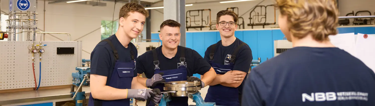 Junge Männer im Blaumann lachen zusammen bei der Arbeit in der Werkstatt