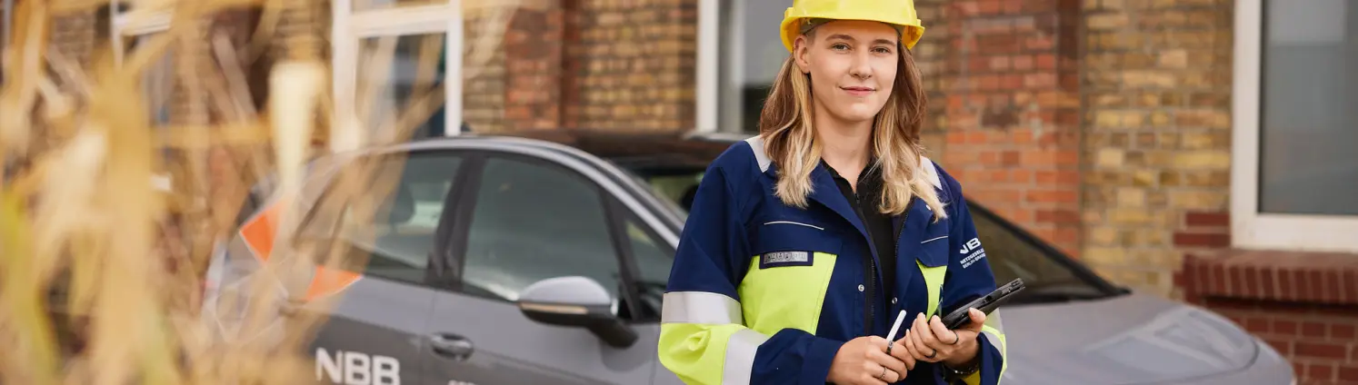 Mitarbeitende Person in Schutzkleidung mit Helm steht vor einem Servicefahrzeug der NBB und hält ein Tablet.