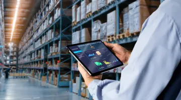 Mann steht in einer Lagerhalle und mit einem Tablet in der Hand