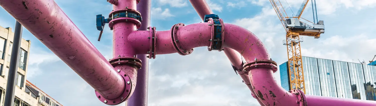 Ein rosa Versorgungsrohr im Vordergrund, eine Baustelle mit Krahn im Hintergrund