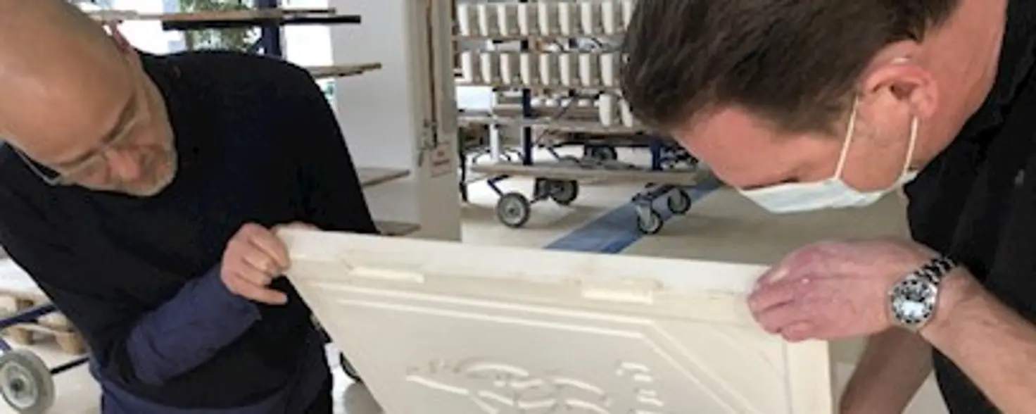 Zwei Männer prüfen eine Porzellan-Tafel, die frisch gegossen wurde