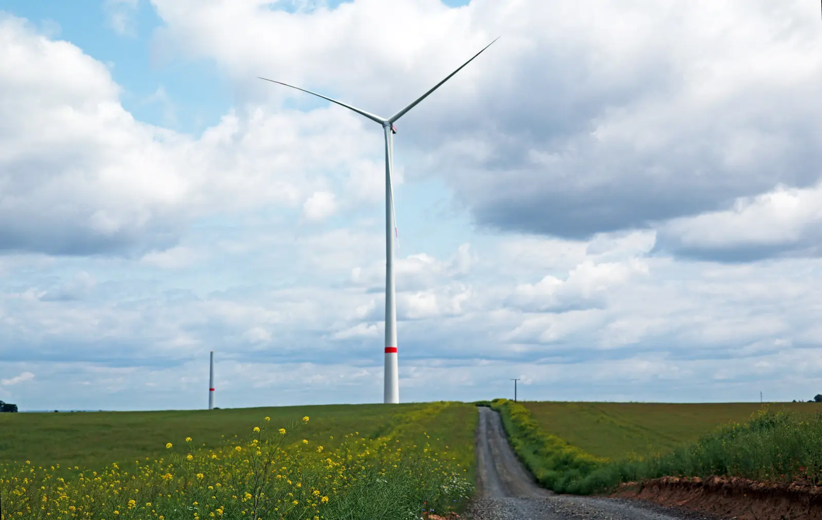 Ein Windrad steht mittig auf einem großen Feld vor bewölktem Himmel.