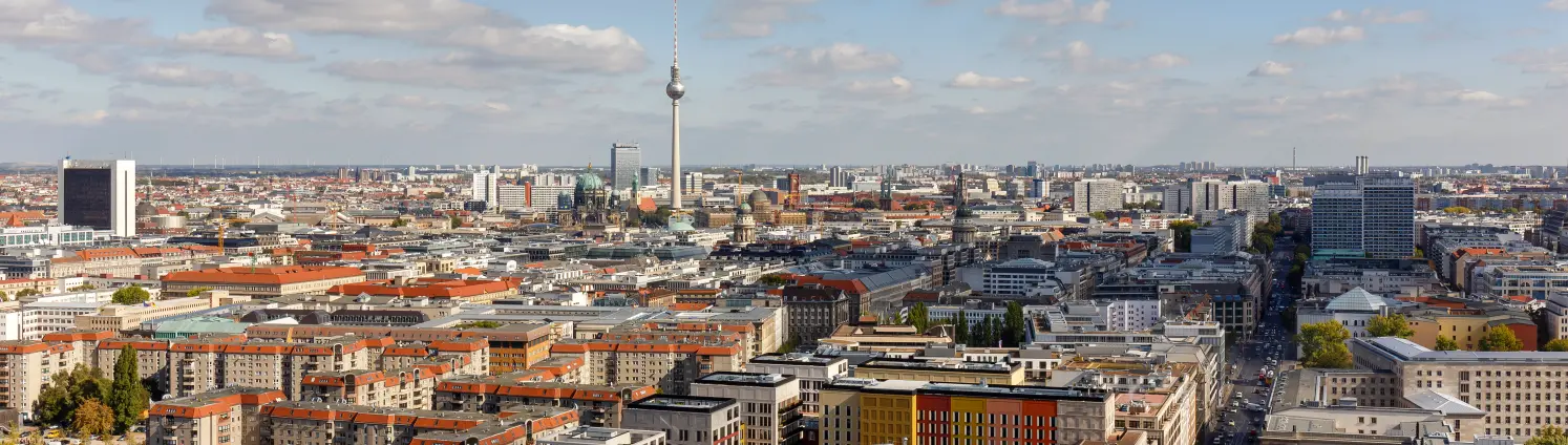 Luftaufnahme von Berlin‑Mitte mit dicht bebauter Innenstadt und dem Fernsehturm am Alexanderplatz im Hintergrund.