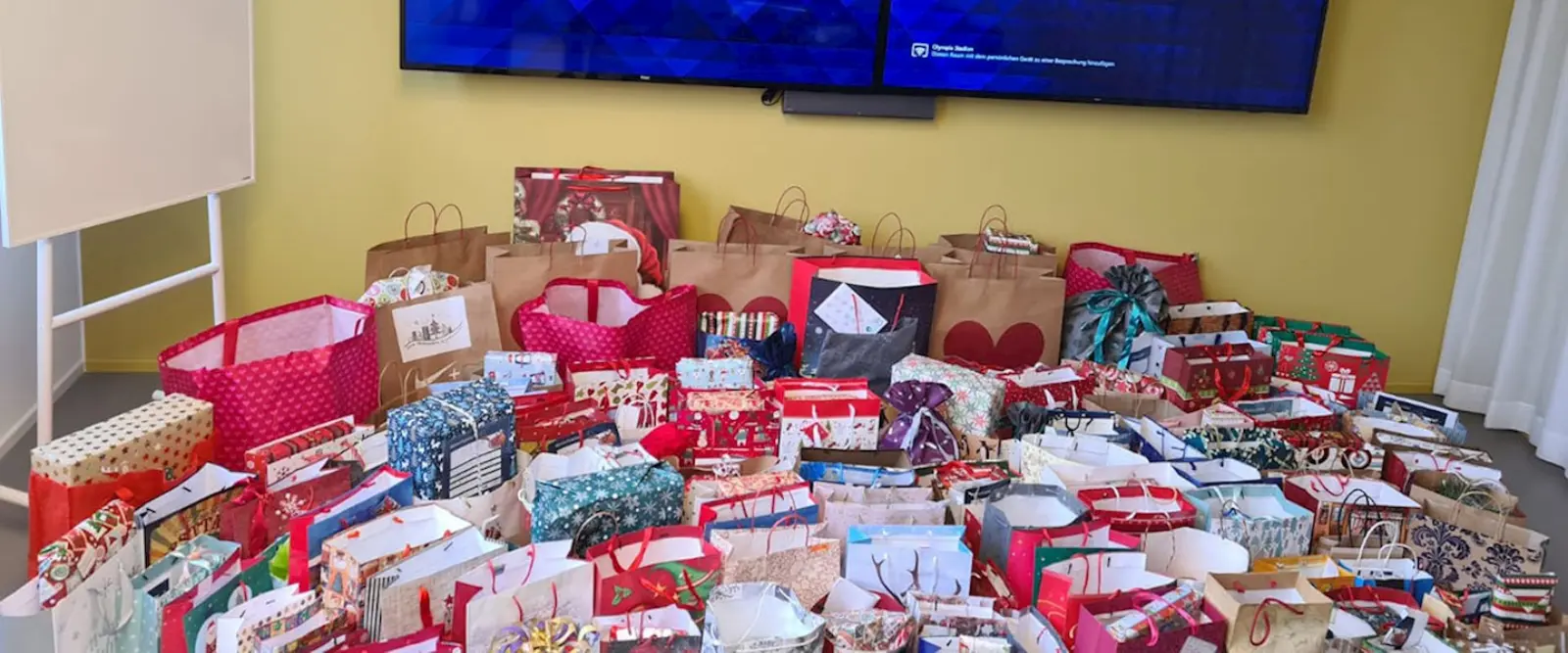 Auf dem Boden steht eine Vielzahl an bunten Geschenktüten, viele in weihnachtlichem Rot