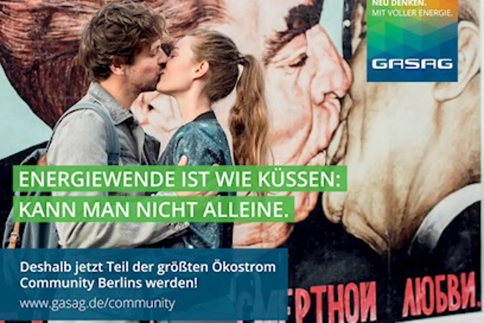 Ein Paar küsst sich vor der Berliner Mauer, auf dem der Bruderkuss zu sehen ist.