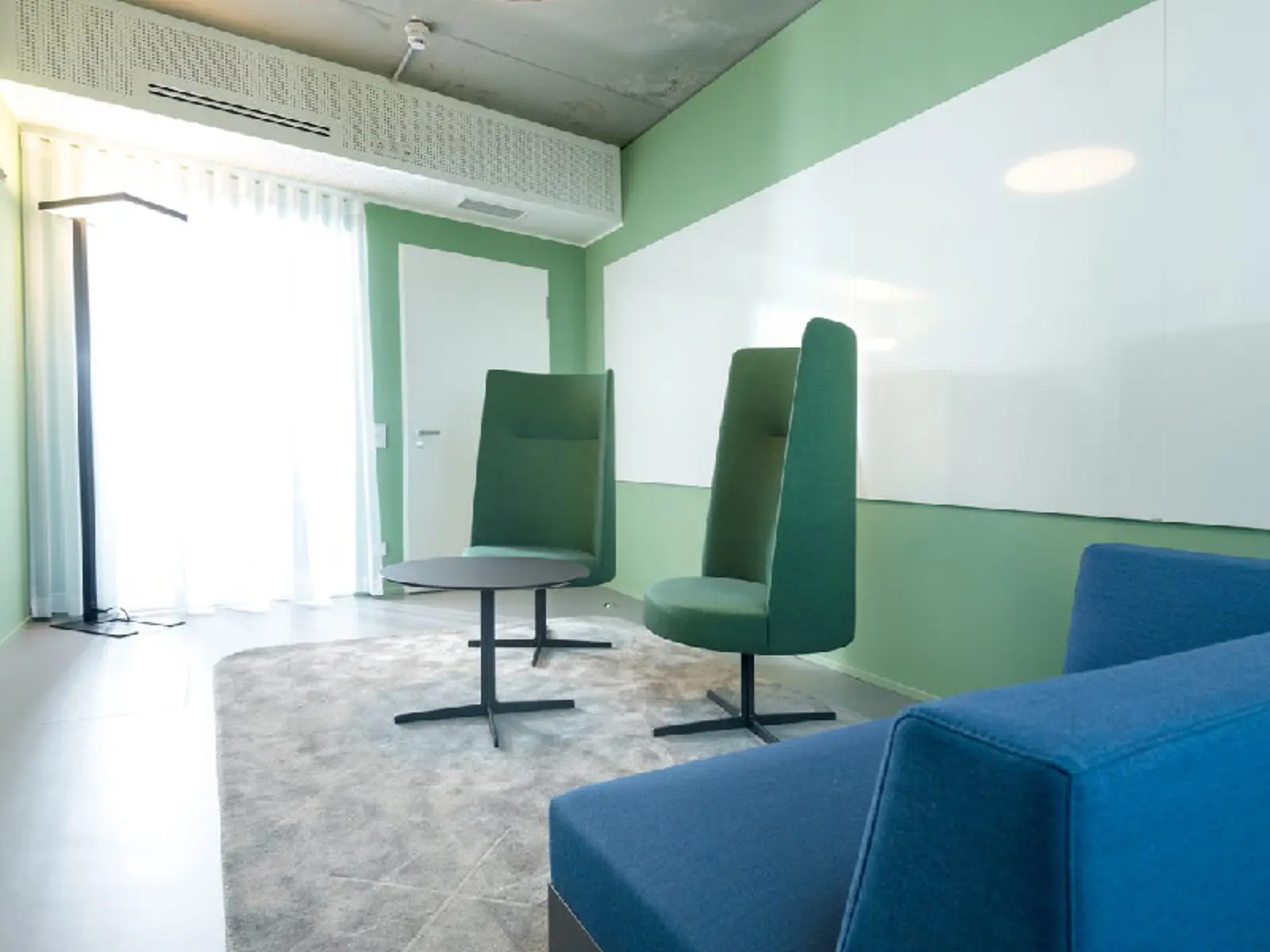 Zwei Sessel und ein kleiner Tisch stehen in einem Besprechungsraum vor einer grünen Wand