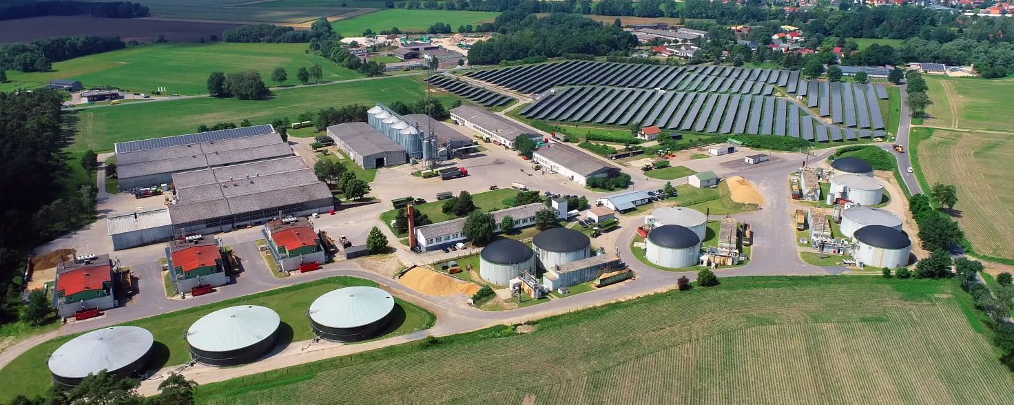 Luftansicht der Biogasanlage im brandenburgischen Putlitz bei blauem Himmel. Drumherum grüne Felder. Bild mit KI erstellt.