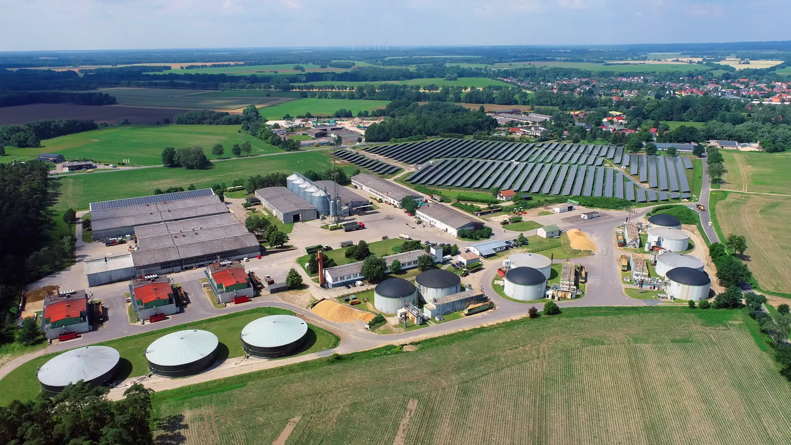 Luftansicht der Biogasanlage im brandenburgischen Putlitz bei blauem Himmel. Drumherum grüne Felder.