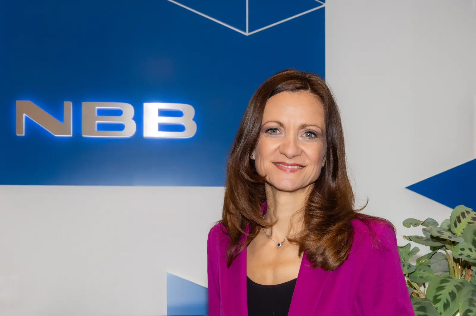 Person in pinkem Blazer vor NBB-Logo auf blauem Hintergrund