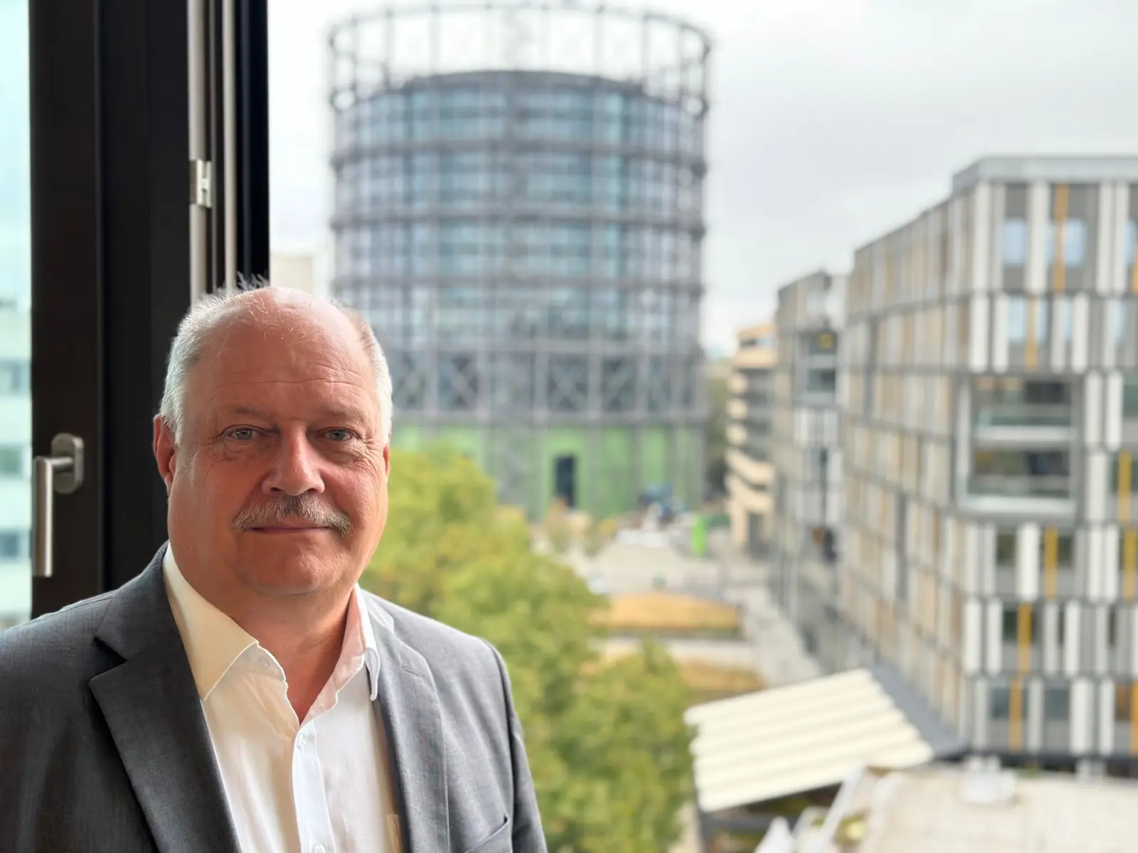 Frank Behrend im grauen Anzug und im Hintergrund das Gasometer in Berlin-Schöneberg