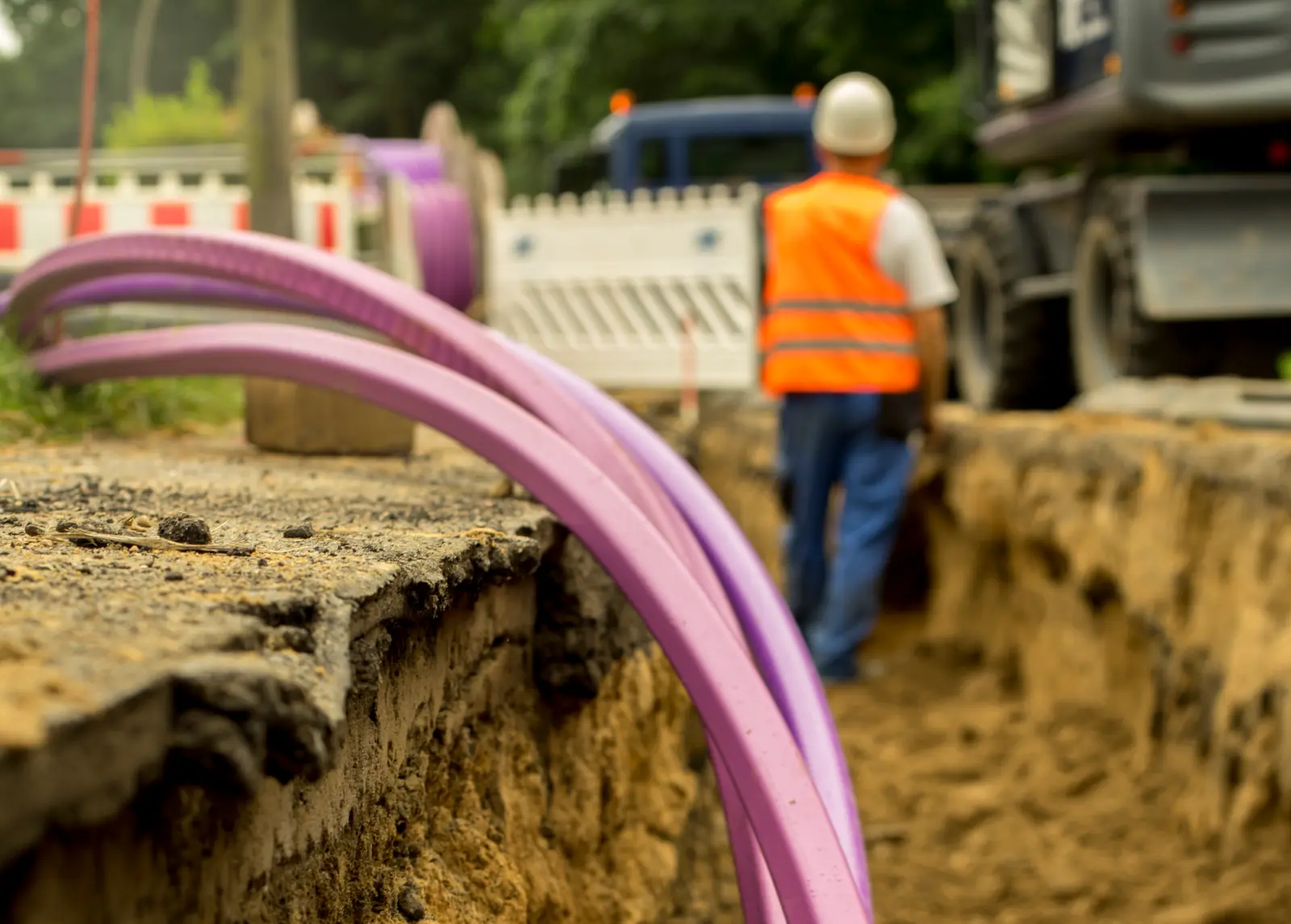 Breitbandausbau: Neues Glasfaserkabel wird in einem Graben verlegt. Im Hintergrund ein Bagger.