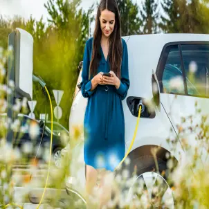 Eine Frau im blauen Kleid steht vor einem weißen E-Auto, das gerade lädt