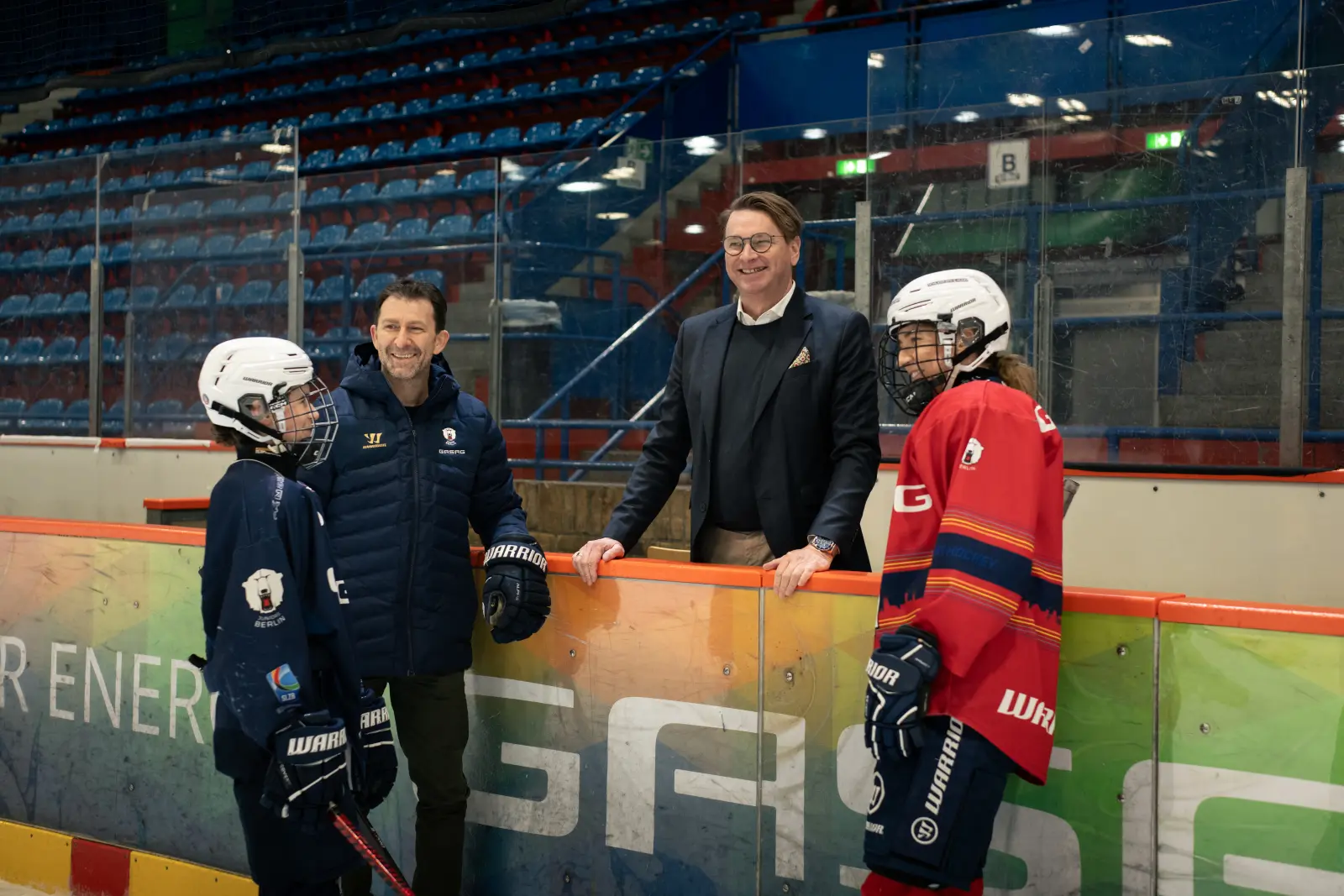 Matthias Trunk, Vorstandsmitglied von GASAG, und Sven Felski von den Eisbären Berlin unterhalten sich mit Eishockey-Spielerinnen und Spielern.