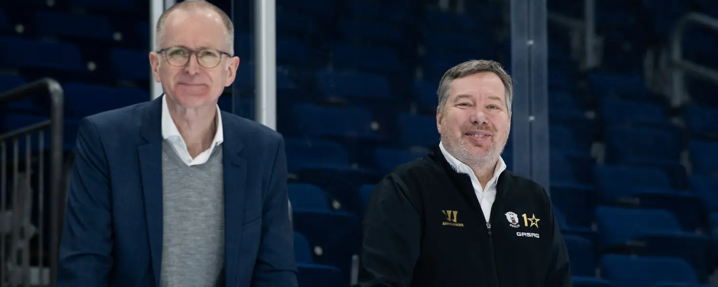 Georg Friedrichs, GASAG-Vorstandsvorsitzender, und Thomas Bothstede, Geschäftsführer der EHC Eisbären Berlin, stützen sich auf die Bande im Stadion.