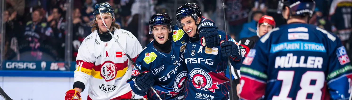 Spieler der Eisbären Berlin jubeln nach einem Sieg und liegen sich auf der Eisfläche in den Armen.