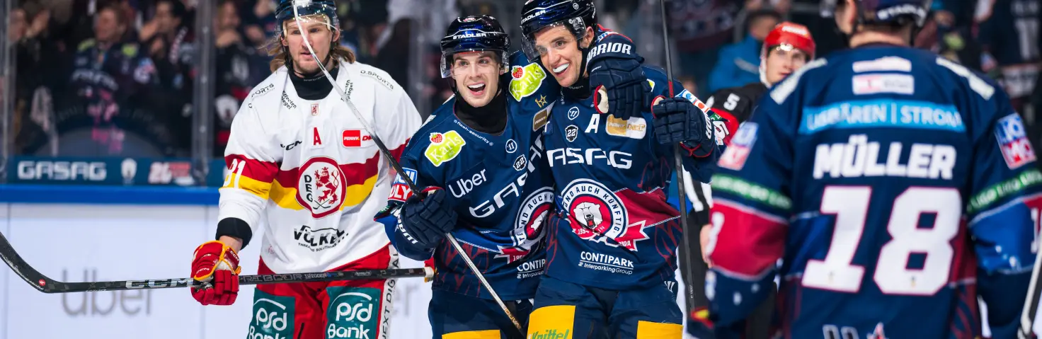 Spieler der Eisbären Berlin jubeln nach einem Sieg und liegen sich auf der Eisfläche in den Armen.