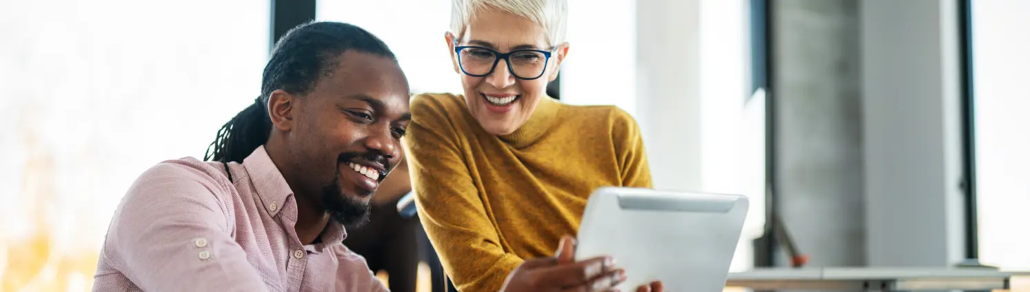 Ein Kollege mit Dreadlocks zeigt einer älteren Kollegin im Rollstuhl einen Projektentwurf auf dem Tablet-Computer.